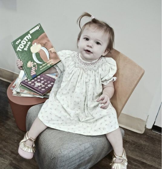 Toddler girl holding The Tooth Book while visiting children's dentist in Jacksonville