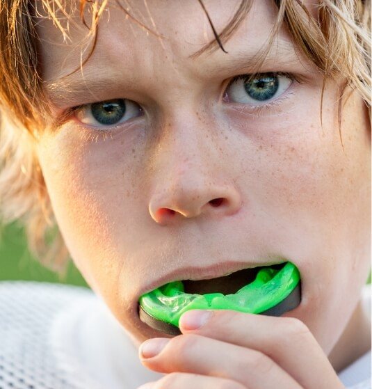 Young boy placing green athletic mouthguard in his mouth