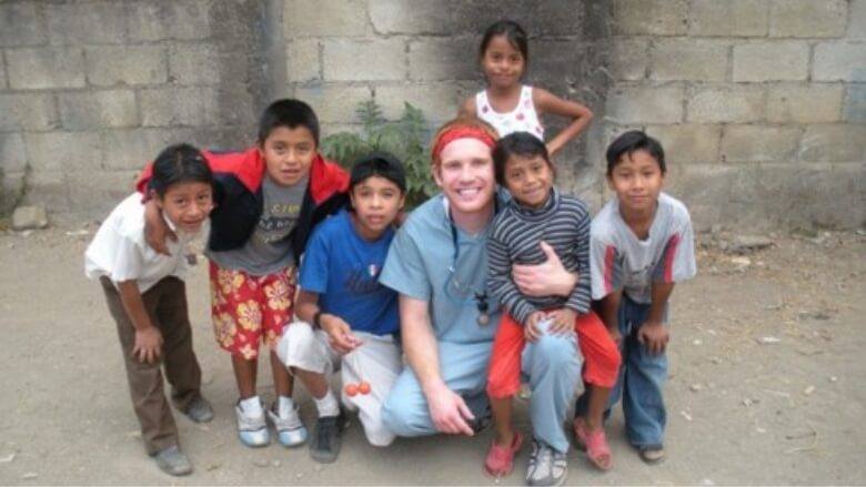 Doctor Altenbach smiling with group of children in front of gray brick wall