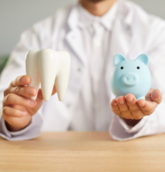 a dentist holding a model tooth and a piggy bank