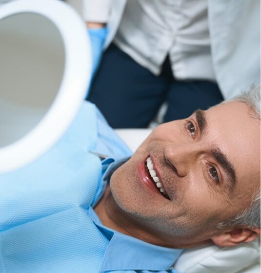 Man viewing his new smile in mirror after smile makeover