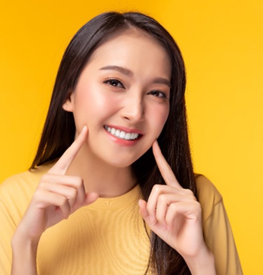 Woman pointing to her smile after receiving cosmetic dentistry in Jacksonville