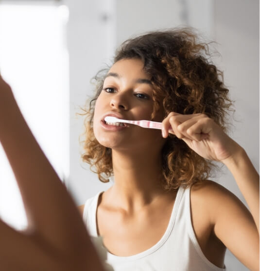 Young woman brushing her teeth in front of mirror