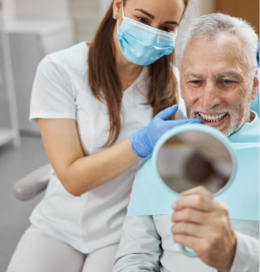 Senior man looking at his smile in a mirror while in dental chair
