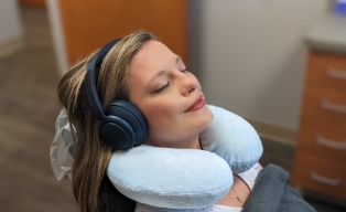 Woman relaxing in dental chair with headphones and neck pillow