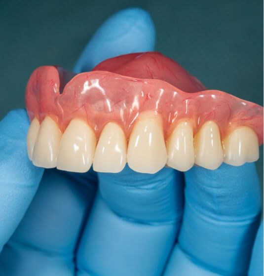 Dentist holding a full upper denture in gloved hand