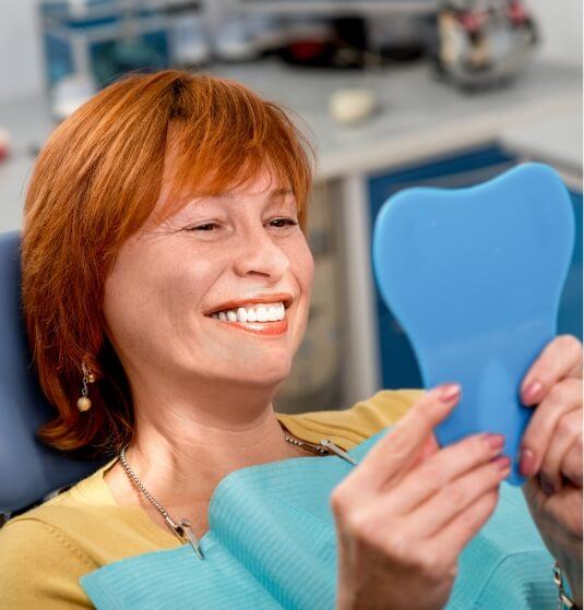 Woman in dental chair seeing her new smile in mirror