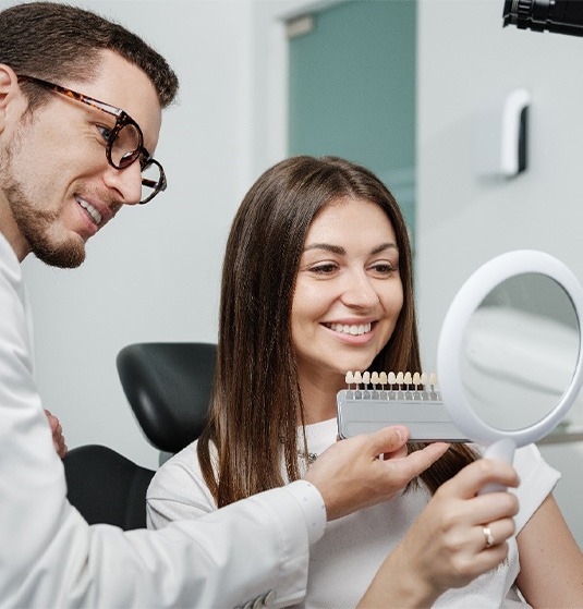 Cosmetic dentist holding shade guide next to a patients smile while they look in a mirror