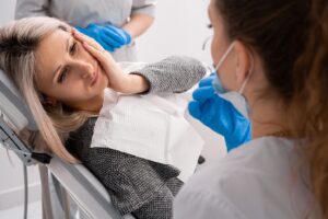 Woman in dentist’s chair holding side of face in pain.